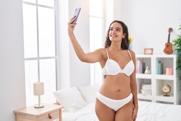 Young beautiful hispanic woman make selfie by smartphone standing at bedroom