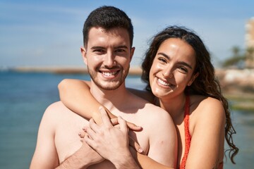 Young hispanic couple tourists wearing swimsuit hugging each other at seaside