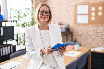 Young caucasian woman working at the office wearing glasses winking looking at the camera with sexy expression, cheerful and happy face.