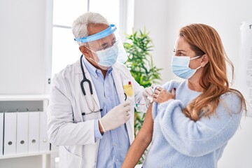 Middle age man and woman doctor wearing medical mask vaccinating patient at clinic