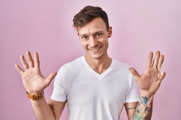 Caucasian man standing over pink background showing and pointing up with fingers number nine while...