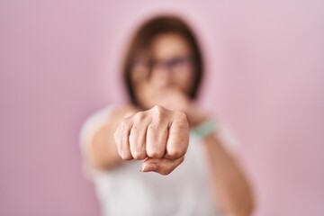 Obraz premium Middle age hispanic woman standing over pink background punching fist to fight, aggressive and angry attack, threat and violence