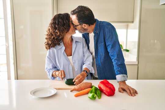 Middle age hispanic couple kissing and hugging each other cooking at kitchen