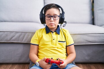 Young hispanic kid playing video game holding controller wearing headphones depressed and worry for distress, crying angry and afraid. sad expression. - Powered by Adobe