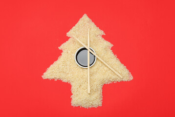 Christmas tree made of raw rice, soy sauce and chopsticks on red background