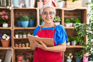 Middle age grey-haired woman florist smiling confident writing on notebook at florist