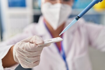 Young beautiful hispanic woman scientist pouring liquid to antigen test at pharmacy