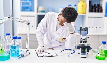 African american woman wearing scientist uniform stressed working at laboratory