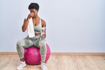African american woman wearing sportswear sitting on pilates ball tired rubbing nose and eyes feeling fatigue and headache. stress and frustration concept.