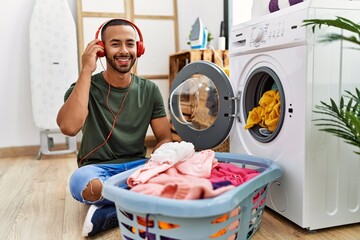 Young hispanic man listening to music using washing machine at laundry