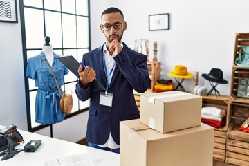 African american man working as manager at retail boutique with hand on chin thinking about...