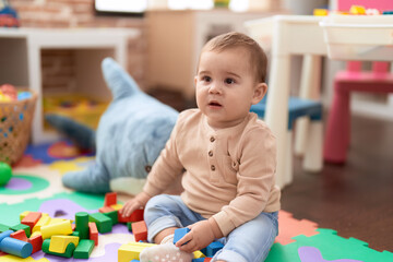 Adorable toddler playing with wooden construction blocks sitting on floor at kindergarten