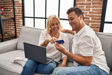 Middle age man and woman using laptop and credit card sitting on sofa at home