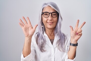 Middle age woman with tattoos wearing glasses standing over white background showing and pointing up with fingers number eight while smiling confident and happy.