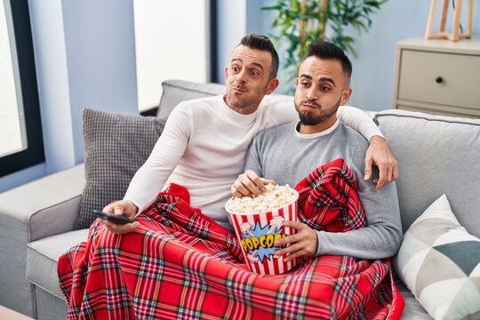 Homosexual Couple Eating Popcorn Watching Tv Puffing Cheeks With Funny Face. Mouth Inflated With Air, Catching Air.