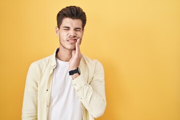 Young hispanic man standing over yellow background touching mouth with hand with painful expression because of toothache or dental illness on teeth. dentist