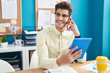 Young hispanic man business worker talking on smartphone using touchpad at office