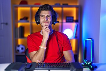 Young hispanic man playing video games looking confident at the camera with smile with crossed arms...
