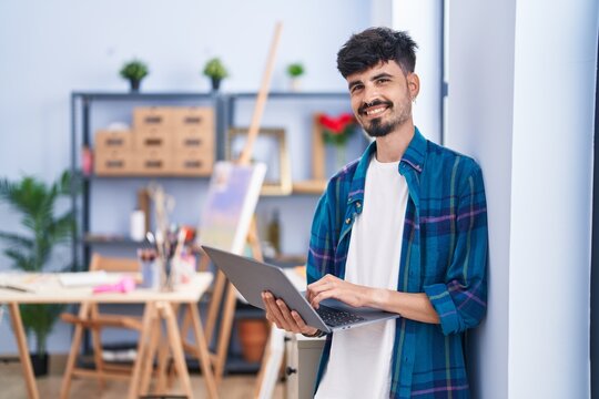 Young hispanic man artist smiling confident using laptop at art studio