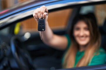 Young hispanic woman smiling confident holding key of new car at street