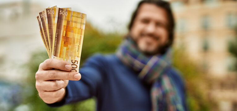 Middle age handsome man holding norwegian krone banknotes outdoors at the park