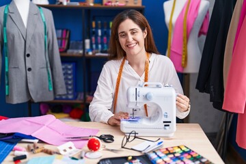 Young woman tailor smiling confident using sewing machine at sewing studio