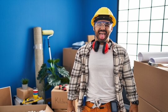 Young Hispanic Man With Beard Working At Home Renovation Sticking Tongue Out Happy With Funny Expression. Emotion Concept.