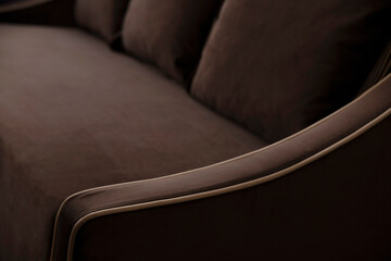 Defocused blurred background of a brown sofa with cushions and beige edging on the elbow of soft fleecy velor. Upholstered furniture close-up in deep shadows with copy space.