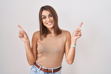 Young hispanic woman standing over white background smiling confident pointing with fingers to different directions. copy space for advertisement
