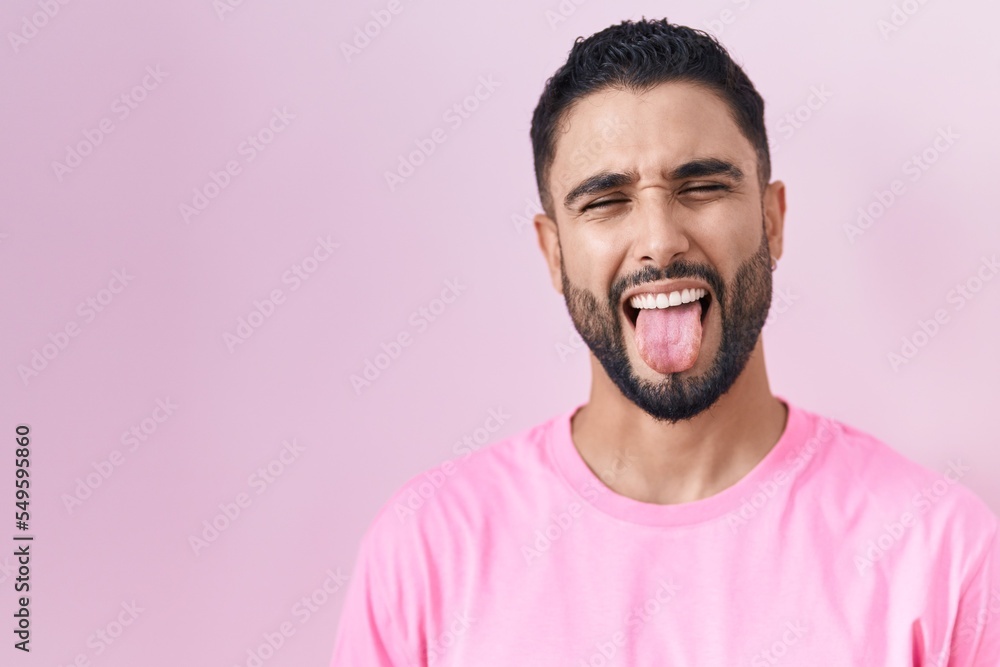 Sticker Hispanic young man standing over pink background sticking tongue out happy with funny expression. emotion concept.