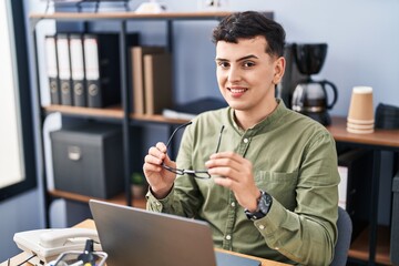 Young non binary man business worker holding glasses using laptop at office