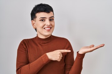 Non binary person wearing make up standing over isolated background amazed and smiling to the camera while presenting with hand and pointing with finger.