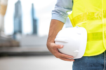 Engineer holding hardhat wearing yellow vest and standing ready for work safety in site.