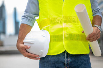 Engineer holding hardhat and floor plan wearing yellow vest and standing ready for work safety in site.