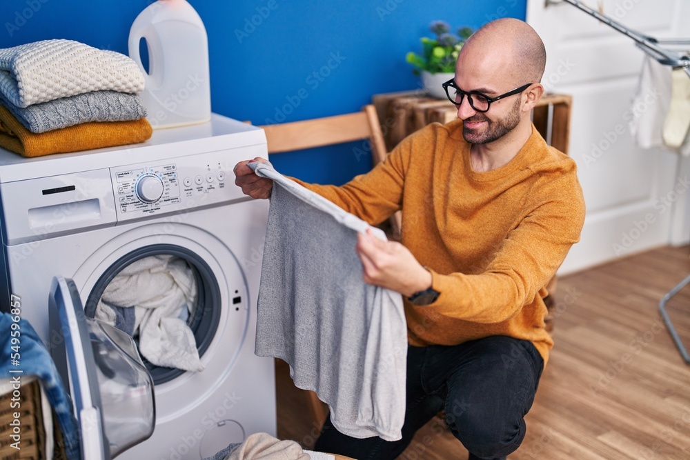 Wall mural Young man smiling confident washing clothes at laundry room