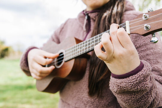 Unrecognizable female person playing ukelele standing on the grass.
