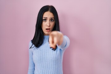 Hispanic woman standing over pink background pointing displeased and frustrated to the camera,...