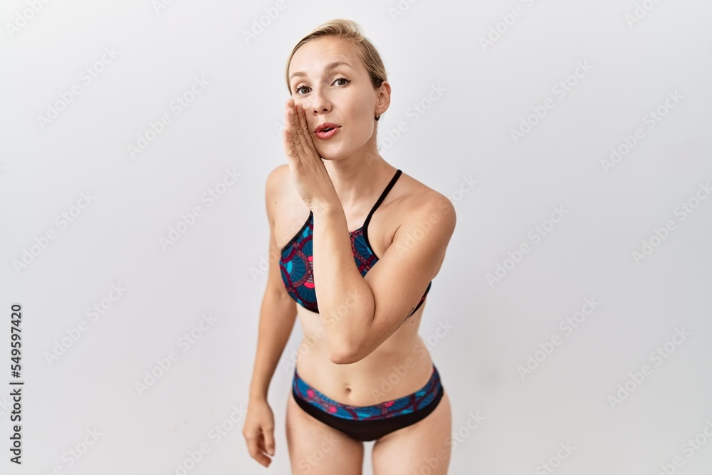 Poster Young blonde woman wearing sporty bikini over isolated background hand on mouth telling secret rumor, whispering malicious talk conversation