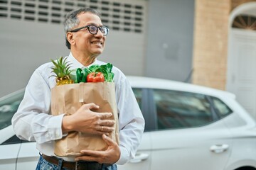 Middle age southeast asian man smiling holding a bag of fresh groceries at the city