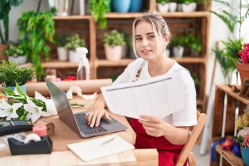 Young blonde woman florist using laptop reading document at flower shop