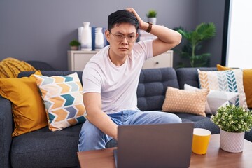Young asian man using laptop at home sitting on the sofa confuse and wondering about question....