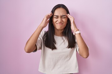 Young hispanic woman standing over pink background with hand on head, headache because stress. suffering migraine.