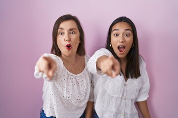 Hispanic mother and daughter together pointing with finger surprised ahead, open mouth amazed expression, something on the front