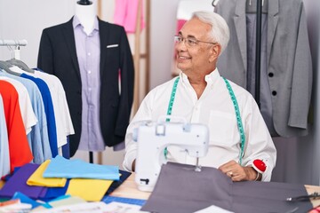 Middle age man with grey hair dressmaker using sewing machine looking away to side with smile on face, natural expression. laughing confident.