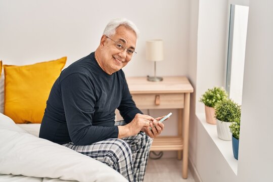Senior man using smartphone sitting on bed at bedroom