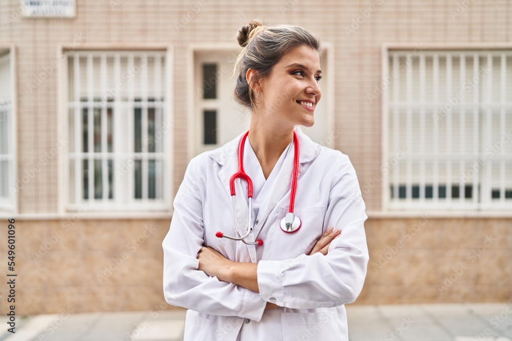 Poster young blonde woman wearing doctor uniform standing with arms crossed gesture at street