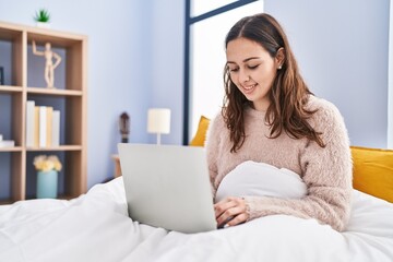 Young beautiful hispanic woman using laptop sitting on bed at bedroom