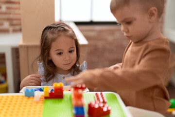 Adorable girl and boy playing with construction block pieces sitting on table at kindergarten