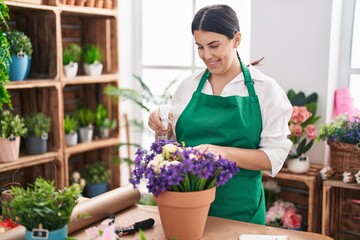 Young beautiful hispanic woman florist using diffuser watering plant at flower shop