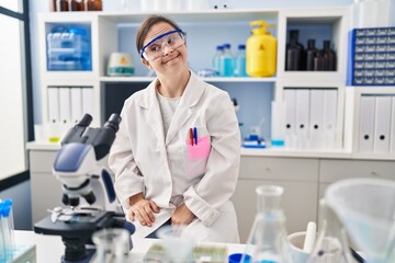 Fototapeta premium Hispanic girl with down syndrome working at scientist laboratory smiling looking to the side and staring away thinking.